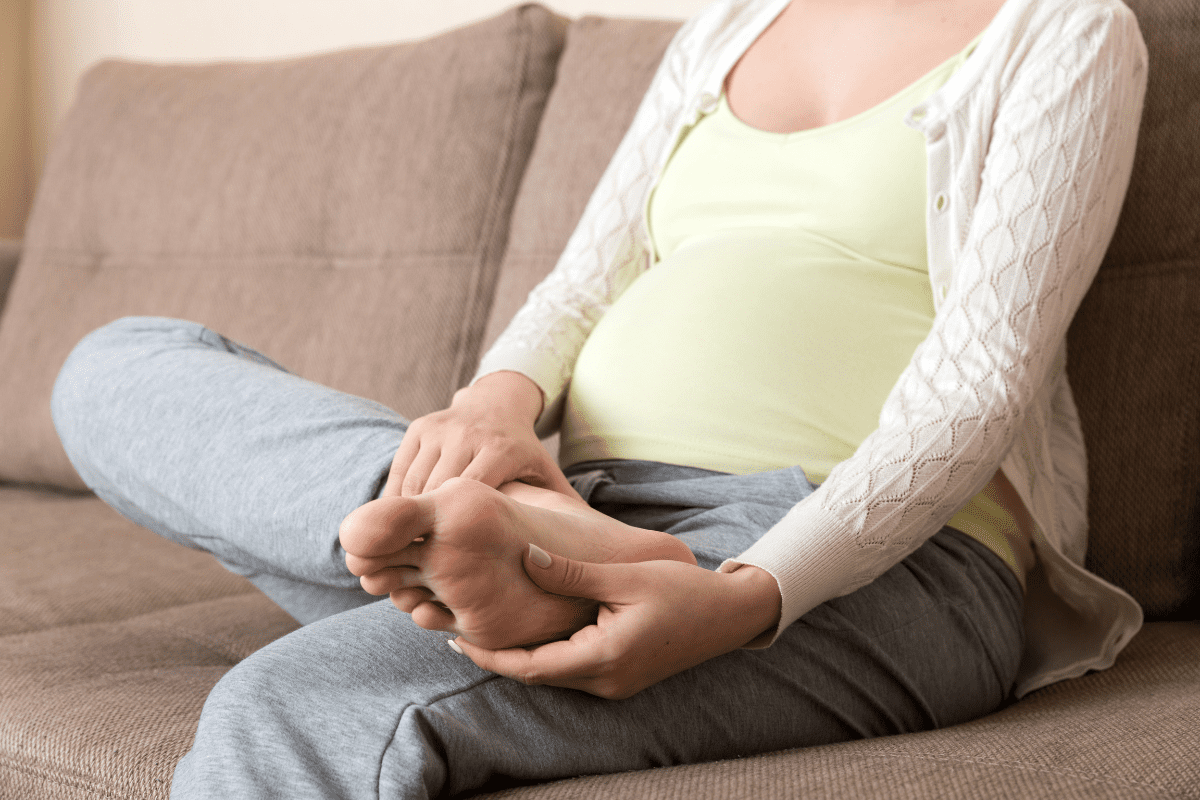 Pregnant person on couch holding and examining foot