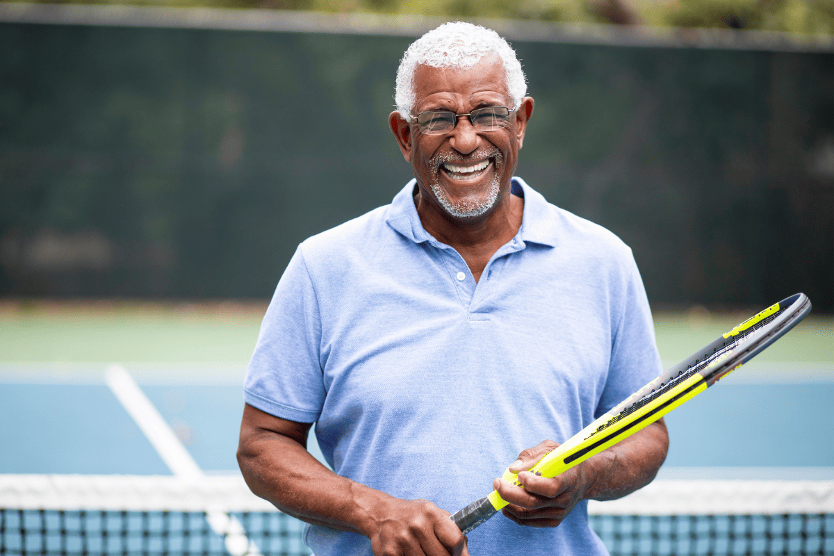 Senior man with grey hair holding tennis rackit on tennis court smiling